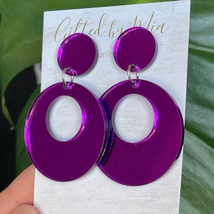 May include: Purple mirrored acrylic earrings with a large circle design. The earrings are on a white card with the text "Gifted by Mia" written in gold.