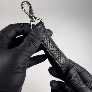 May include: A black leather strap with a silver hook. The strap has a textured, snake-like pattern.