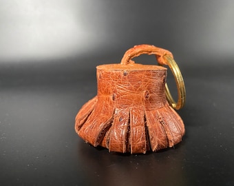 Puede incluir: Un llavero de cuero marrón con un detalle de flecos y un anillo de metal dorado.