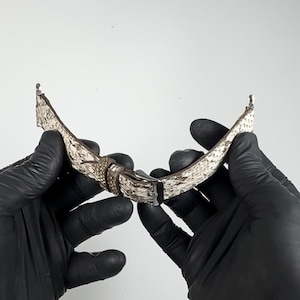 May include: A white and brown leather watch strap with a silver buckle. The strap is designed to look like snakeskin.