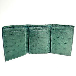 Könnte beinhalten: Eine grüne Lederbörse mit drei Falten, mehreren Kartenfächern und einem Geldfach. Die Börse ist aus Straußenleder mit einem strukturierten Muster.