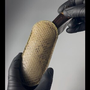 Pode incluir: Uma bainha de faca de couro verde com um padrão texturizado. A bainha é projetada para segurar uma faca dobrável com cabo de madeira.