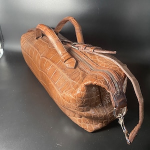 May include: A brown crocodile leather handbag with a top zipper closure and two handles. The bag has a detachable shoulder strap with a silver clasp.
