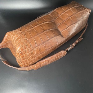May include: A brown crocodile leather handbag with a long strap. The bag has a textured, alligator-like pattern.