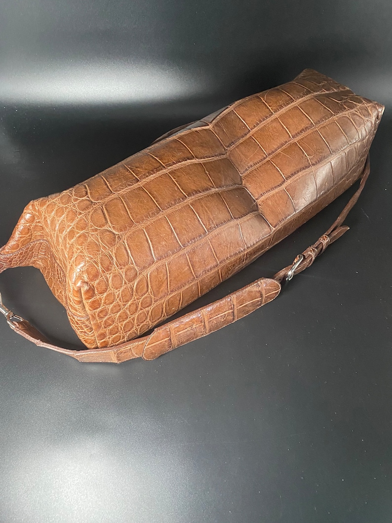 May include: A brown crocodile leather handbag with a long strap. The bag has a textured, alligator-like pattern.