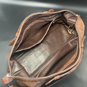 May include: A brown leather travel bag with a crocodile pattern. The bag is open and the inside is lined with brown fabric. The bag has a zipper closure and a shoulder strap.