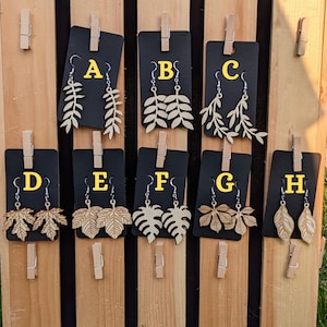 May include: Eight pairs of wooden earrings with different leaf designs. The earrings are displayed on black cards with letters A through H.