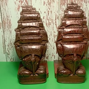 Puede incluir: Par de sujetalibros de barco de madera tallada de color marrón oscuro. Cada sujetalibros representa un velero detallado con múltiples mástiles y velas. Los sujetalibros se asientan sobre una base rectangular, ideal para una temática náutica.