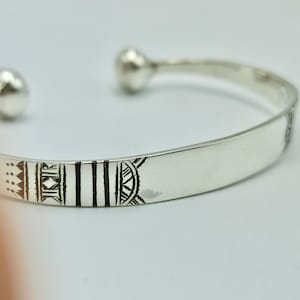 May include: A silver bangle bracelet with a geometric design etched into the surface.