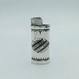 Peut inclure: Briquet en argent avec un motif géométrique. Le briquet présente un motif noir et blanc avec un losange au centre.