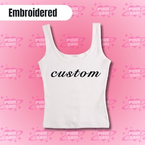 May include: White vest top featuring the word "custom" in black script. The top has a scoop neckline and wide straps. The word "Embroidered" is in a white box at the top.