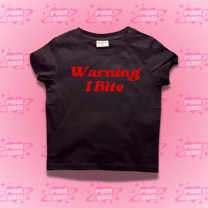 May include: Black t-shirt with red text that says "Warning I Bite" on a pink background with repeating patterns.