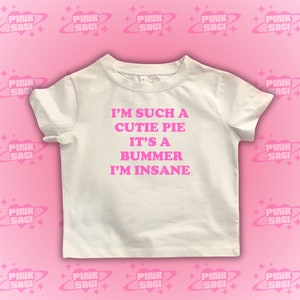 May include: White t-shirt with pink text that reads "I'm such a cutie pie it's a bummer I'm insane."