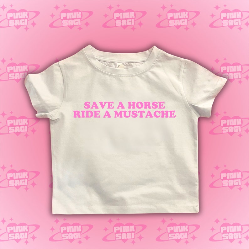 Puede incluir: Camiseta blanca con texto rosa que dice "Save a horse, ride a mustache".
