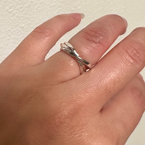 May include: A silver ring with three intertwined bands. The ring is worn on a finger.