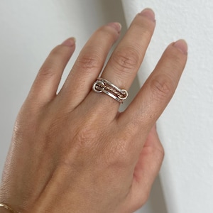Puede incluir: Un anillo de plata y oro con un diseño único entrelazado. El anillo se lleva en el dedo índice de una mano.