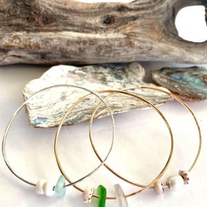 May include: Three gold and silver bangle bracelets with sea glass and pearl accents. The bracelets are stacked on top of each other.