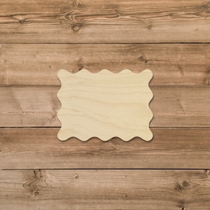May include: A blank, wavy-edged wooden sign with a light brown color. The sign is sitting on a brown wooden surface.