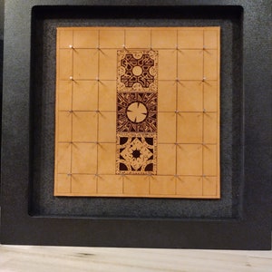 May include: A brown leather board with a grid pattern and three intricate wooden puzzle pieces in the center. The puzzle pieces are in the shape of a square, a circle, and a star. The board is framed in black.
