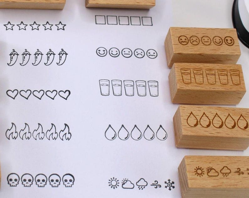 K&ouml;nnte beinhalten: Holzstempel mit verschiedenen Designs, darunter Sterne, Quadrate, Chilischoten, Herzen, Flammen, Totenk&ouml;pfe und Wassergl&auml;ser. Zus&auml;tzliche Stempel zeigen Gesichter mit unterschiedlichen Ausdr&uuml;cken, Wassertropfen und Wettersymbolen. F&uuml;r Bastelarbeiten und Journale.