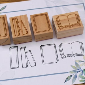 K&ouml;nnte beinhalten: Holzstempel mit Buchmotiven. Die Stempel sind rechteckig mit ge&auml;tzten Buchillustrationen. Unter den Stempeln befinden sich passende Buchumrisse. Der Hintergrund ist ein wei&szlig;es Papier mit floralem Design.