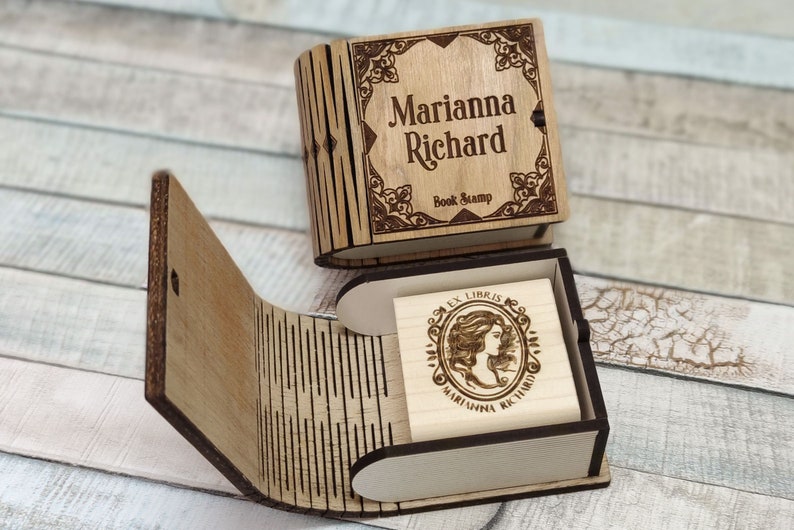 以下が含まれることがあります： 木製のブックスタンプボックス。蓋には「Marianna Richard Book Stamp」という個人名入り。ボックスが開いており、木製のスタンプが露出。スタンプには「Ex Libris Marianna Richard」という文字と装飾的なデザインが刻まれている。