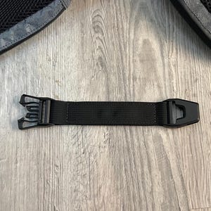 May include: A close-up of a black backpack strap with a plastic buckle. The strap is made of a durable, woven material. The buckle is designed to securely fasten the strap.
