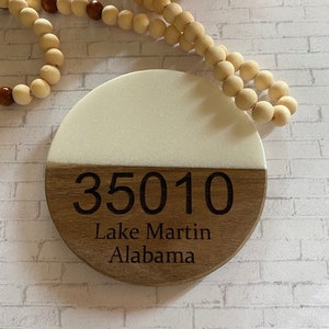 May include: A round wooden sign with a white top half and a brown bottom half. The sign has the number 35010, the words "Lake Martin" and "Alabama" engraved on it.