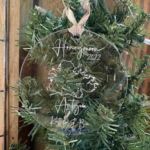 May include: A clear round ornament with the text "Honeymoon 2022" and a map of Antigua. The ornament also includes the names "Kaitlin & Ben".