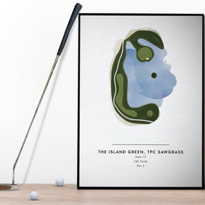 May include: A framed print of the Island Green, Hole 17 at TPC Sawgrass, with a watercolor-style map in green and blue. The text below indicates the hole is 132 yards, Par 3. A golf putter and golf balls are in the foreground.