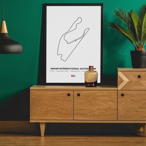 Puede incluir: Una impresi&oacute;n en blanco y negro enmarcada del mapa de la pista del Aut&oacute;dromo Internacional de Miami, exhibida sobre un mueble de madera. Una botella de vidrio decorativa y una planta en maceta est&aacute;n sobre el mueble. Una l&aacute;mpara colgante negra cuelga del techo.