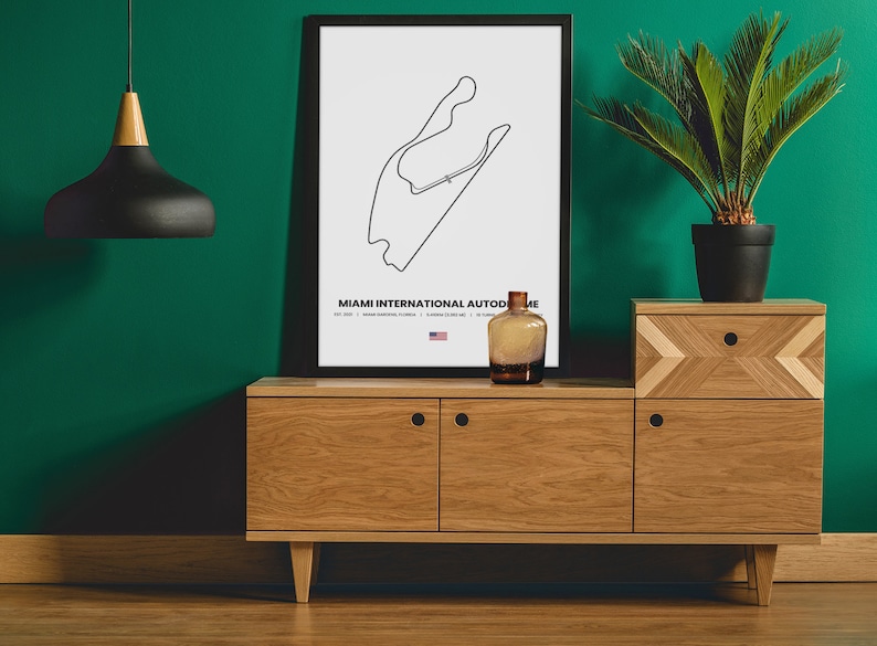 Puede incluir: Una impresi&oacute;n en blanco y negro enmarcada del mapa de la pista del Aut&oacute;dromo Internacional de Miami, exhibida sobre un mueble de madera. Una botella de vidrio decorativa y una planta en maceta est&aacute;n sobre el mueble. Una l&aacute;mpara colgante negra cuelga del techo.