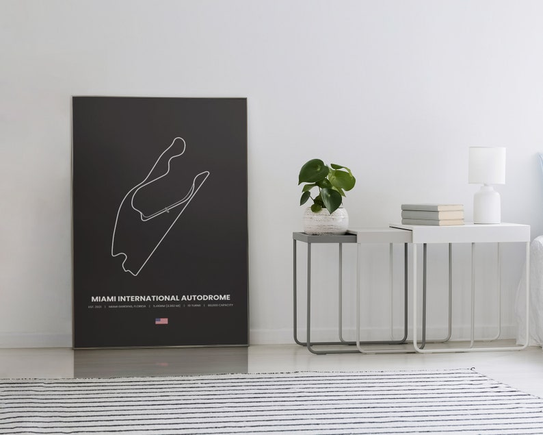 Puede incluir: Un p&oacute;ster negro con un contorno blanco del circuito del Aut&oacute;dromo Internacional de Miami. El p&oacute;ster incluye el nombre de la pista, detalles y una peque&ntilde;a bandera estadounidense. El p&oacute;ster se exhibe en una habitaci&oacute;n con mesas auxiliares, una l&aacute;mpara y una planta.