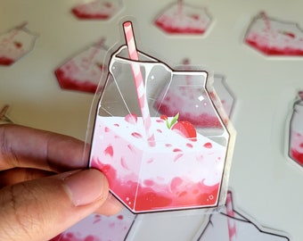 Op de afbeelding: Een transparante sticker van plastic van een melkpak gevuld met een roze en rode aardbeienmelk drank met een rood-wit gestreepte rietje.