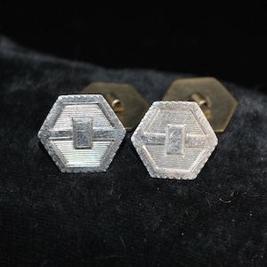 May include: A pair of vintage silver cufflinks with a geometric design. Each cufflink has a hexagonal shape with a rectangular centre and horizontal lines. The backs are gold in colour.