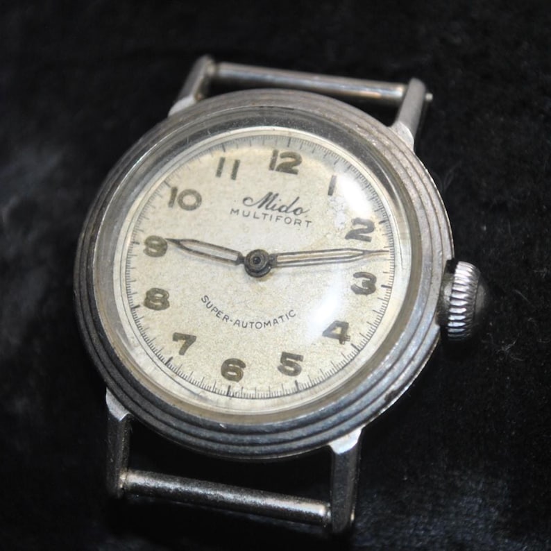 Pu&ograve; includere: Orologio da polso vintage Mido Multifort Super-Automatic con cassa color argento e quadrante color crema. Il quadrante presenta numeri arabi e lancette nere. L'orologio ha una corona strutturata e attacchi per cinturino in acciaio inossidabile.