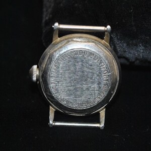 Pu&ograve; includere: Primo piano del retro di un orologio da polso vintage color argento. Il quadrante dell'orologio &egrave; rotondo, con le parole "MIDO MULTIFORT SUPERAUTOMATIC" e altro testo attorno al bordo. Ha una corona argentata e un attacco per cinturino argentato.