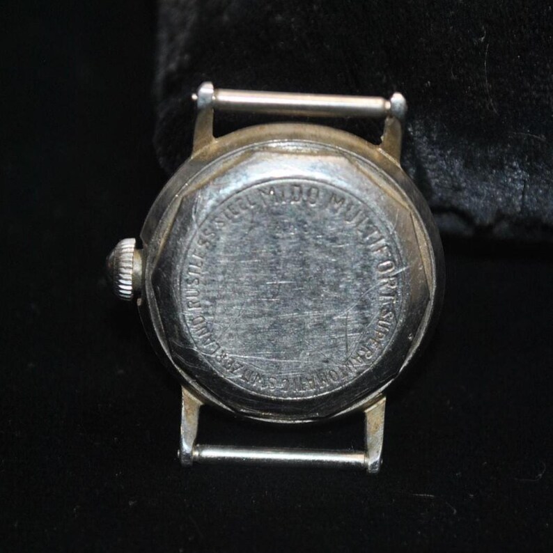 Pu&ograve; includere: Primo piano del retro di un orologio da polso vintage color argento. Il quadrante dell'orologio &egrave; rotondo, con le parole "MIDO MULTIFORT SUPERAUTOMATIC" e altro testo attorno al bordo. Ha una corona argentata e un attacco per cinturino argentato.