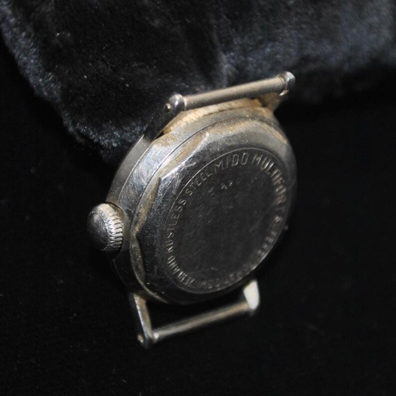 Pu&ograve; includere: Primo piano di un orologio da polso vintage argentato. L'orologio ha un quadrante rotondo con una corona strutturata e un retro in acciaio inossidabile. Sono visibili gli attacchi del cinturino. L'orologio &egrave; su uno sfondo scuro.