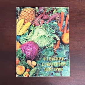 May include: A vintage cookbook with a colorful cover featuring a variety of fruits and vegetables. The title of the book is "Blender Liquefier Recipes".