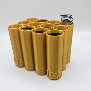 May include: A gold-colored 3D printed battery holder with 12 individual slots for batteries. A black spring is on top of the holder.