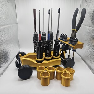 May include: A gold-colored tool organizer shaped like a race car with a variety of tools, including screwdrivers, pliers, and a set of gold-colored rings.