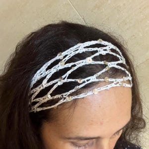 May include: A white crocheted headband featuring a delicate, open-weave net pattern. The accessory is embellished with small, circular, reflective silver sequins spaced throughout the yarn, creating a subtle shimmer across the entire design.