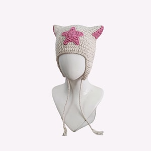 May include: A white crocheted hat with pink star detail and ear flaps. The hat has long ties that can be tied under the chin.