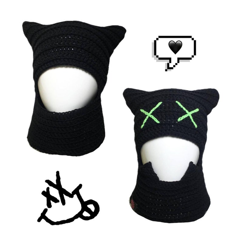 May include: Two black crochet cat hats with green embroidered details. One hat has a simple design, while the other has two green X's on the front. Both hats have a face opening and a neck flap.