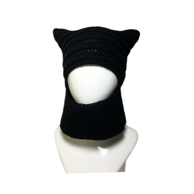 May include: Black crocheted cat ear hat with a face opening and a neck warmer. The hat is on a white mannequin.