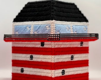 May include: A red, white, and blue tissue box cover with a black roof and a black railing. The cover is made of plastic canvas and is decorated with a striped pattern.