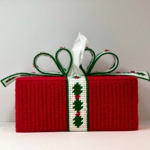 May include: Red tissue box cover with a white and green holly design and a white bow. The cover is made of a woven fabric.