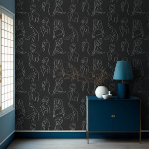 Peut inclure: Papier peint gris foncé avec un motif répété de figures blanches dessinées au trait dans diverses poses. Une lampe bleue avec un abat-jour et un meuble bleu avec des bordures dorées sont au premier plan. Un vase et un bol blancs sont sur le meuble.