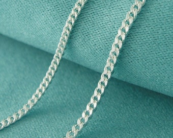 May include: A silver chain necklace on a teal fabric background.